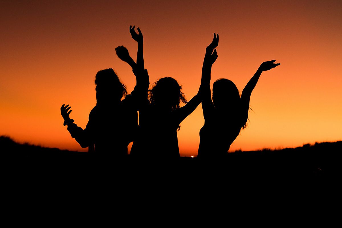 3 people celebrating in silhouette against a sunset